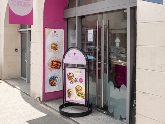 Törtchen Törtchen Die Fassade von "Törtchen Törtchen" in Köln mit einem großen, pinken Bogen und einladendem Schaufenster.