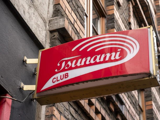 Tsunami Club You can see a red and white sign with the words "Tsunami Club" on the wall of a building.