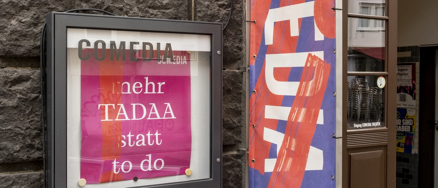 Comedia The entrance to the Comedia theaters in Cologne displays colorful flags and an illuminated poster inviting passers-by to discover the lively cultural scene.