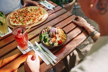 Stadtgarten Ein bunt gedeckter Holztisch zeigt einen sommerlichen Tisch im Freien mit einem frischen Salat und Pizza.