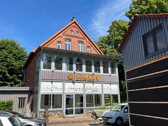 KreativWerkstatt am Wall Ein Backsteingebäude mit großen Fenstern und verzierten Holzdetails bei sonnigem Wetter.