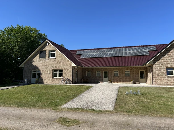 Campingplatz Emstal Sustrum ©Emsland Tourismus GmbH (1).jpeg Backsteingebäude mit rotem Dach und Solaranlage auf gepflegtem Gelände unter klarem blauem Himmel