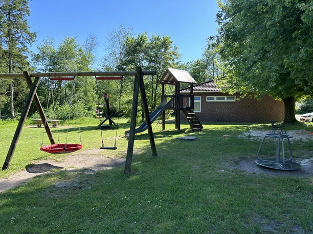 Campingplatz Hotel Zur Emsbrücke©Emsland Tourismus GmbH (3).jpeg Spielplatz auf dem Campingplatz mit Schaukeln, Rutsche und Karussell unter blauem Himmel.