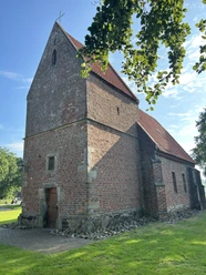 Kapelle Bückelte ©Emsland Tourismus GmbH (8).jpeg Backsteinkapelle mit rotem Satteldach und Holztür, umgeben von Grün und blauem Himmel