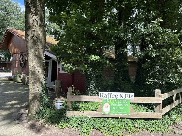 Holzhaus im Grünen mit Schild „Kaffee & Eis Dreive In – Frische Eier & mehr bei Fam. Wiggerthale“.