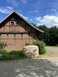 Hof Lindemann Heimatverein Gersten ©Emsland Tourismus GmbH (1).JPEG Backsteinscheune mit Fachwerk, davor Stein mit Inschrift Hof Lindemann unter blauem Himmel.