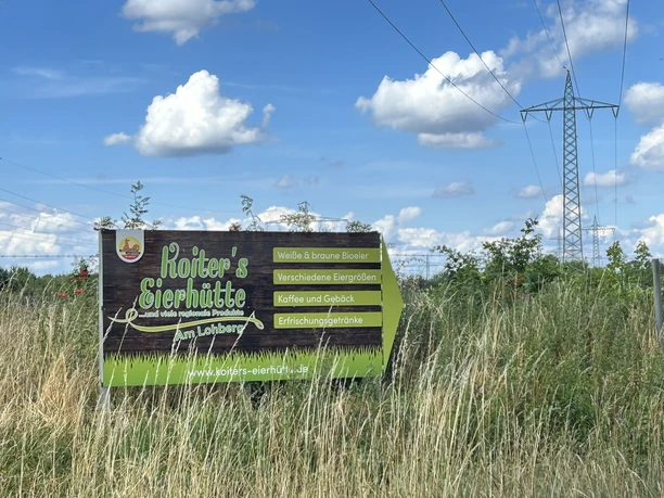Koiters Eierhütte, Meppen Am Lohberg ©Emsland Tourismus GmbH (5).JPEG Werbeschild von Koiters Eierhütte in Meppen vor blauem Himmel und leicht bewölkter Landschaft