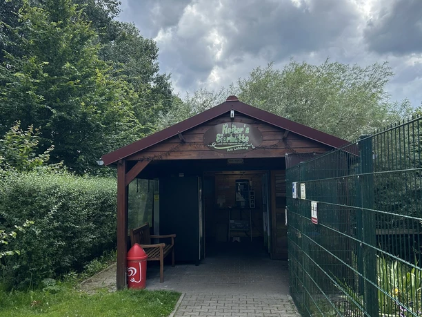 Koiters Eierhütte, Meppen Am Lohberg ©Emsland Tourismus GmbH (6).JPEG Holzhütte mit Verkaufseingang, Bank und rotem Briefkasten unter wolkenverhangenem Himmel