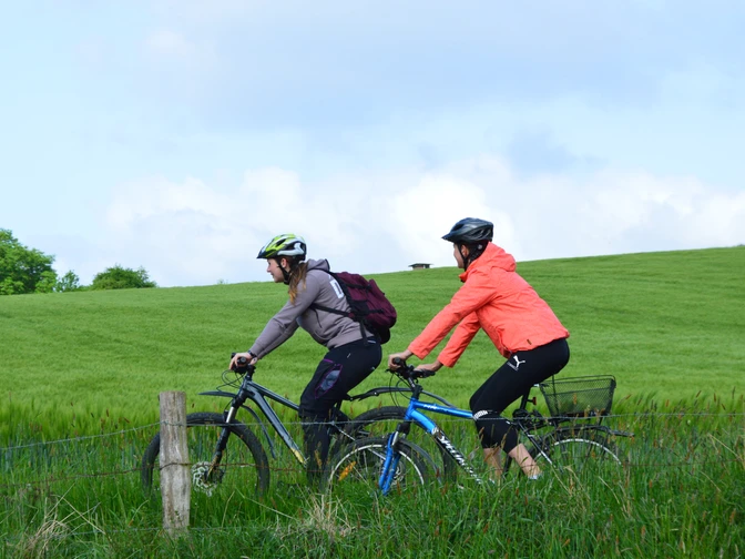 Zwei Radfahrer mit Helmen genießen eine Fahrt auf einem grünen Weg bei bewölktem Himmel.