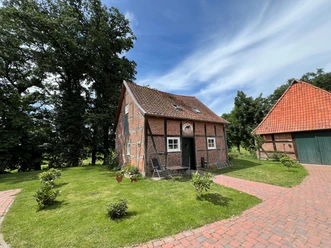 A traditional half-timbered house with red bricks, surrounded by green lawns and trees.