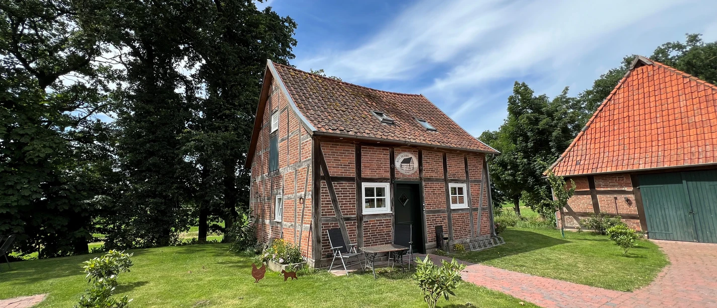 A traditional half-timbered house with red bricks, surrounded by green lawns and trees.