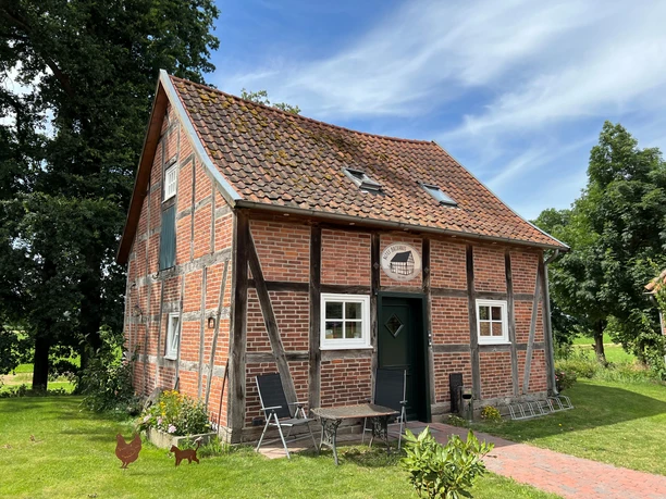 A traditional half-timbered house with red bricks and garden furniture on a green lawn.