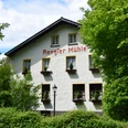 Rengser Mühle Rengser Mühle in Gummersbach, weißes Fachwerkhaus umgeben von üppigem Grün, blauer Himmel.