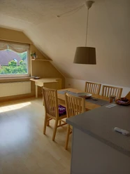 Ferienwohnung Schwarz.jpg Helles, gemütliches Dachgeschosszimmer mit Esstisch, Stühlen, Fensterblick auf grüne Landschaft.