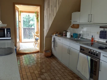 Helle Küche mit L-förmiger Arbeitsplatte, weißen Schränken, Fensterausblick auf grünen Balkon.