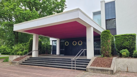 Der Eingang des Neuen Theaters Espelkamp mit modernen Linien und umgeben von gepflegter Bepflanzung.