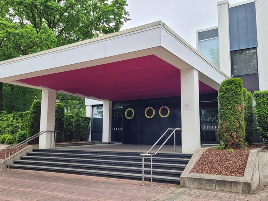 Der Eingang des Neuen Theaters Espelkamp mit modernen Linien und umgeben von gepflegter Bepflanzung.