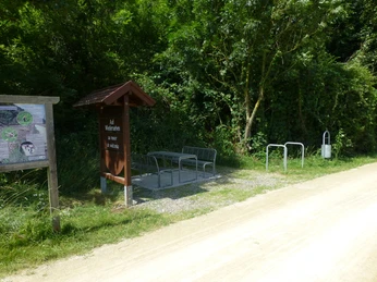P1120757.JPG Drei Metallbänke stehen an einem Schotterweg, umgeben von üppigem Grün und angrenzendem Wald.