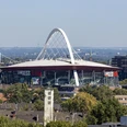 Lanxess Arena Lanxess Arena, ein riesiger roter Kuppelbau mit markantem weißen Bogenträger in Köln.