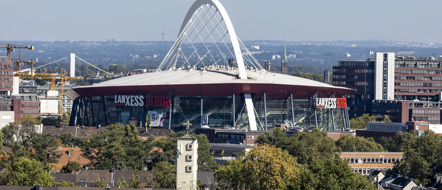 Lanxess Arena Lanxess Arena, ein riesiger roter Kuppelbau mit markantem weißen Bogenträger in Köln.