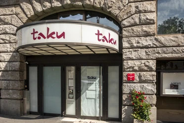 Eingang des eleganten Restaurants Taku mit Steinmauerwerk und einer modernen Glasfront.