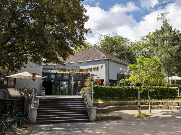 Cafe Friedolin BuezE Decorated terrace with a festive garland in front of the Ehrenfeld community center with a park around it.