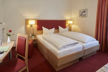 Doppelzimmer im Hotel zur Traube in Velbert Helles Doppelzimmer mit zwei Einzelbetten, rotem Teppichboden, Schreibtisch und einer roten Rose.