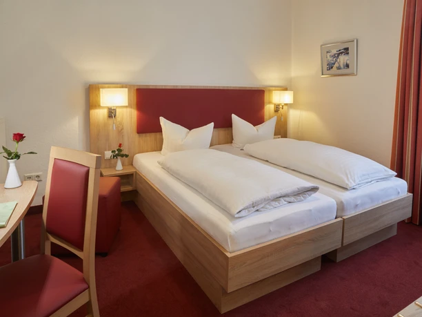 Doppelzimmer im Hotel zur Traube in Velbert Helles Doppelzimmer mit zwei Einzelbetten, rotem Teppichboden, Schreibtisch und einer roten Rose.