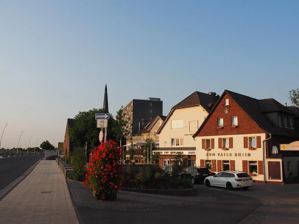 Das Hotel & Restaurant Zum Vater Rhein in der Abendsonne, Monheim am Rhein Gastronomie und Hotellerie am Rhein, im Abendlicht von Monheim gelegen mit roten Blumen im Vordergrund.