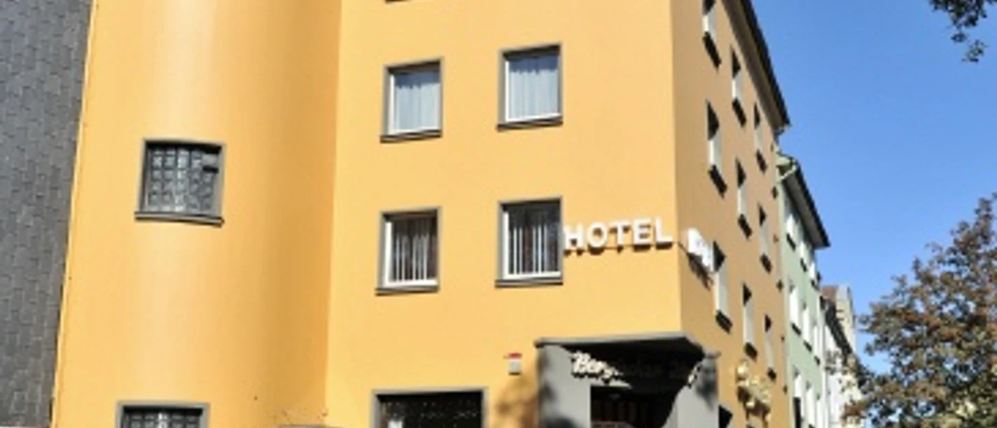 Hotel und Restaurant Bergischer Hof in Ratingen Ein vierstöckiges, senfgelbes Hotel mit markantem Rundturm und rechteckigen Fenstern in Ratingen.