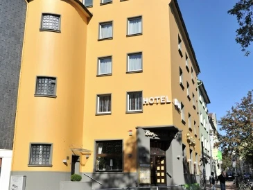 Hotel und Restaurant Bergischer Hof in Ratingen Ein vierstöckiges, senfgelbes Hotel mit markantem Rundturm und rechteckigen Fenstern in Ratingen.