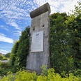 Ein originales Mauerstück der Berliner Mauer, umgeben von grüner Vegetation und einem Infobereich.