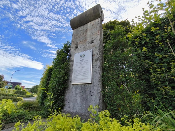 Berliner Mauerstück in Riege Ein originales Mauerstück der Berliner Mauer, umgeben von grüner Vegetation und einem Infobereich.