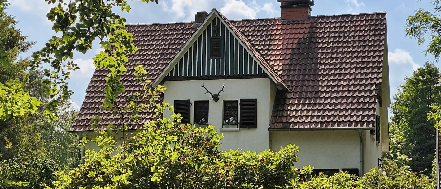 Sattes Grün umgibt das Forsthaus Hövelhof mit einem Giebel und roten Ziegeldach unter blauem Himmel.
