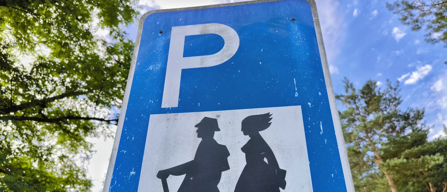 Wanderparkplatz Hövelhof Parkschild mit Wanderermotiv in grüner Umgebung, Himmel im Hintergrund, an Ort Hövelhof positioniert.