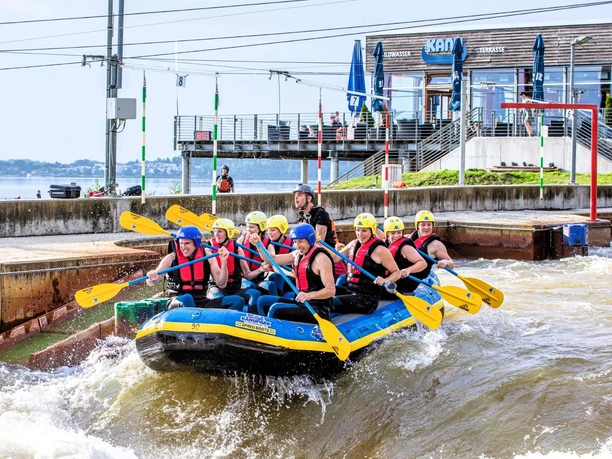 Nine people sit with helmets and paddles in a rafting boat in the Markkleeberg canoe park, white water, leisure, water sports