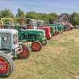 Auf Achse 2022 Eine Reihe bunter Oldtimer-Traktoren steht auf einem Feld, umrahmt von Bäumen und Schaulustigen.