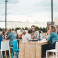 Wine festival on the Rhine Menschen sitzen an Holztischen im Freien, genießen Getränke, vor einer urbanen Kulisse.People sit at wooden tables outdoors, enjoying drinks, against an urban backdrop.