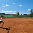 Tennis Club Großenheidorn Eine Frau spielt Tennis auf einem Sandplatz unter blauem Himmel, im Hintergrund sind Häuser.