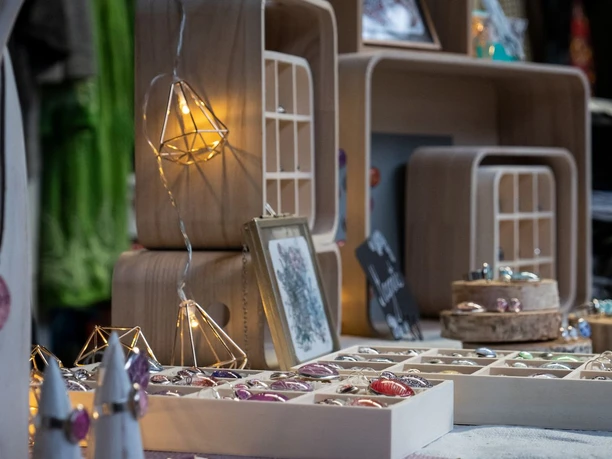Verschiedene handgefertigte Schmuckstücke in Holzkästen vor einem Marktstand arrangiert.