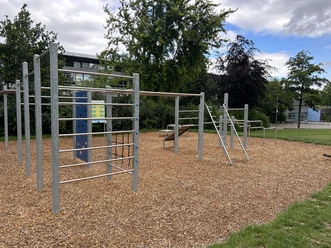 Calisthenics facility | Büren Outdoor-Sportplatz mit Klettergerüsten auf Rindenmulch, umgeben von Bäumen und Rasenfläche.