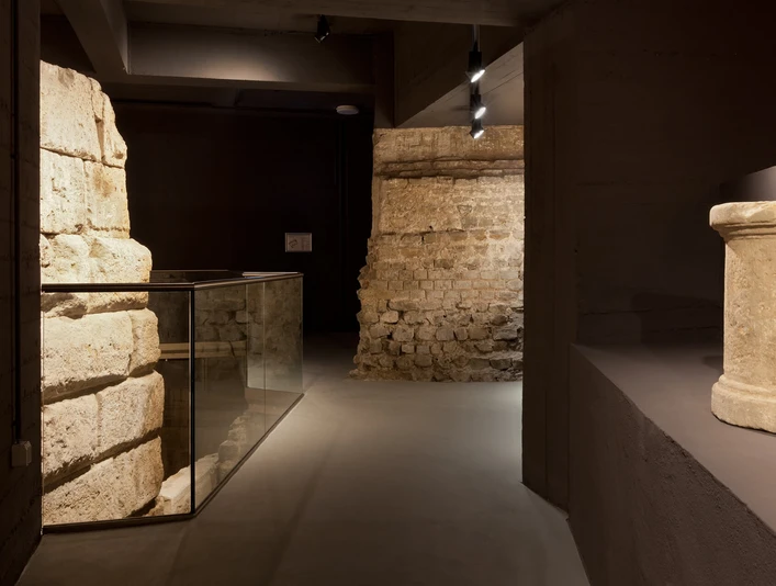 Ubiermonument Im Bild sind historische Mauerwerke aus dem antiken Ubiermonument in Köln zu sehen. Im Vordergrund ein Zylinder, dahinter hell beleuchtete Steinwände, die die archäologische Atmosphäre unterstreichen.The picture shows historical masonry from the ancient Ubiermonument in Cologne. In the foreground is a cylinder, behind it brightly lit stone walls that emphasize the archaeological atmosphere.