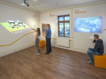 Römergrab Weiden In einem Museumsraum zeigen Projektoren historische Bilder und Texte an weißen Wänden.In a museum room, projectors show historical images and texts on white walls.