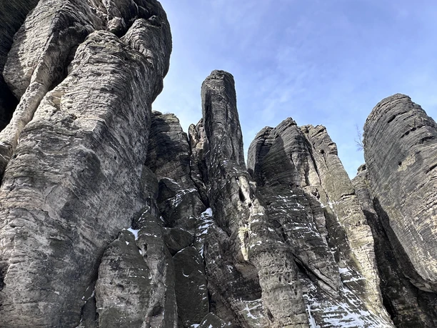 High, jagged rock formations with scattered remnants of snow against a clear blue sky.