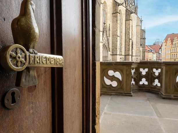 Rathaus Osnabrück Tür mit dekorativem Türgriff neben steinernem Balkon und historischen Gebäuden im Hintergrund.