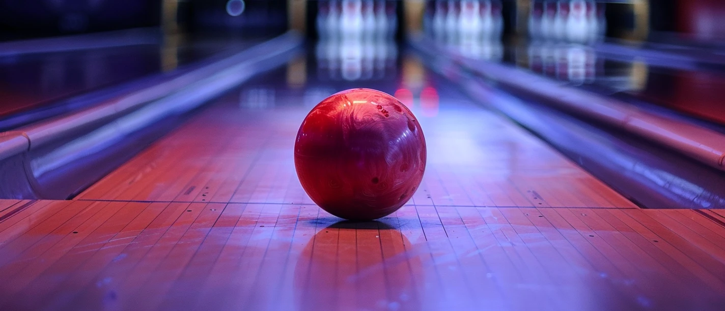 Red bowling ball on an illuminated lane, blurred bowling pins in the background. The atmosphere is calm and concentrated.