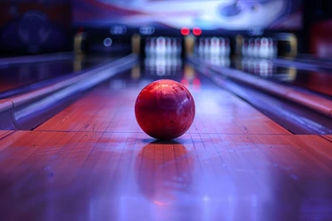 Bowlingbahn Palla da bowling rossa su una pista illuminata, birilli sfocati sullo sfondo. L'atmosfera è calma e concentrata.