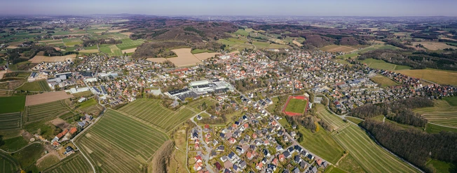 Luftaufnahme einer weitläufigen, grünen Landschaft mit einer Kleinstadt und umgebenden Hügeln.