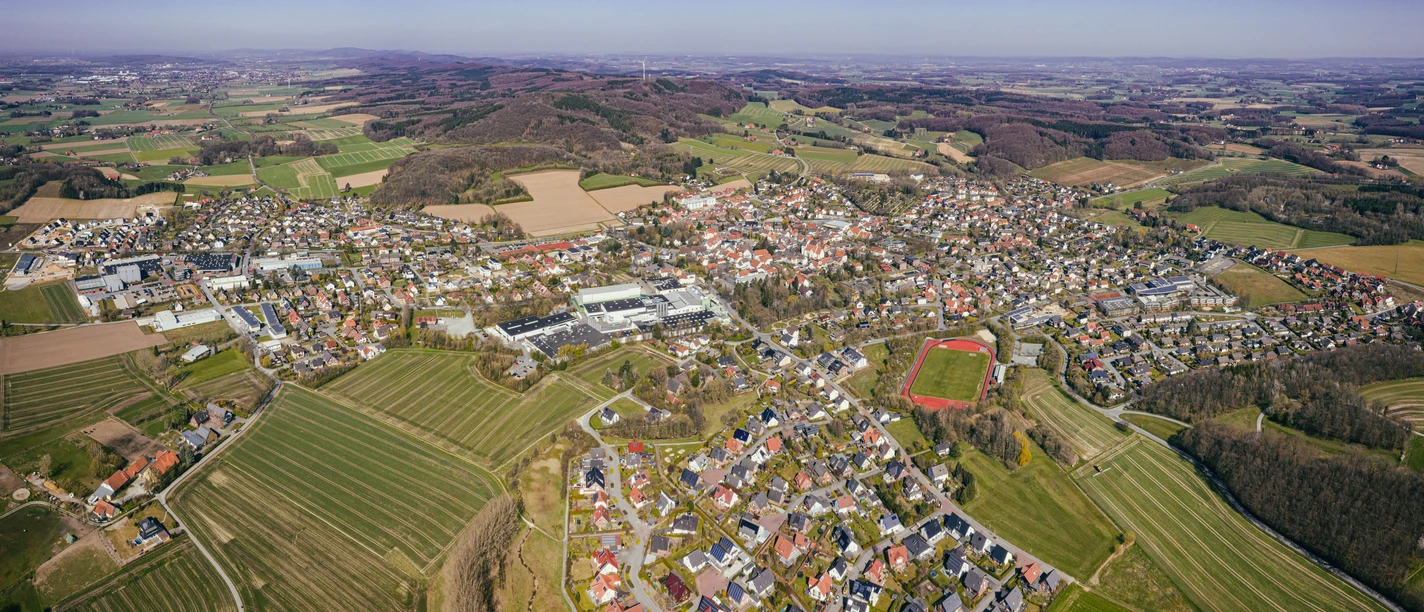 Luftaufnahme einer weitläufigen, grünen Landschaft mit einer Kleinstadt und umgebenden Hügeln.