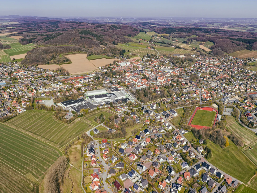 Panorama Borgholzhausen_EDIT.jpg Luftaufnahme einer weitläufigen, grünen Landschaft mit einer Kleinstadt und umgebenden Hügeln.
